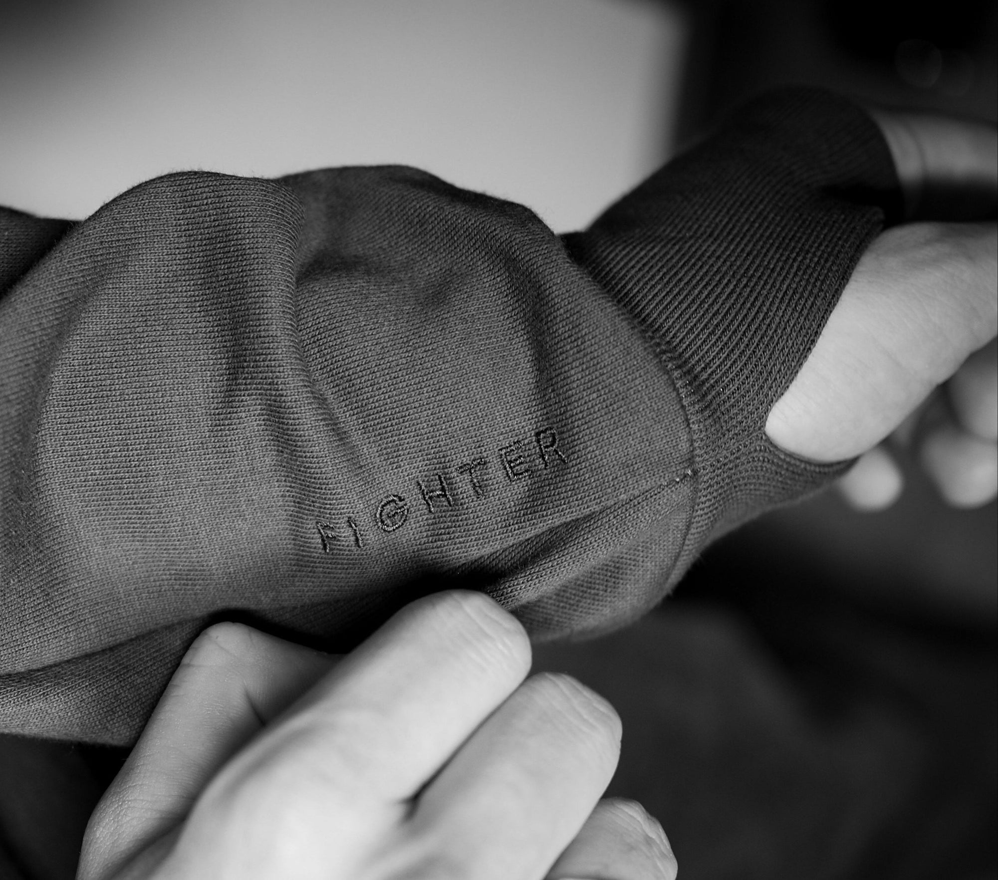Close-up of a person adjusting a hoodie sleeve with hidden thumbholes and embroidered letters 'FIGHTER' right beside the cuff.